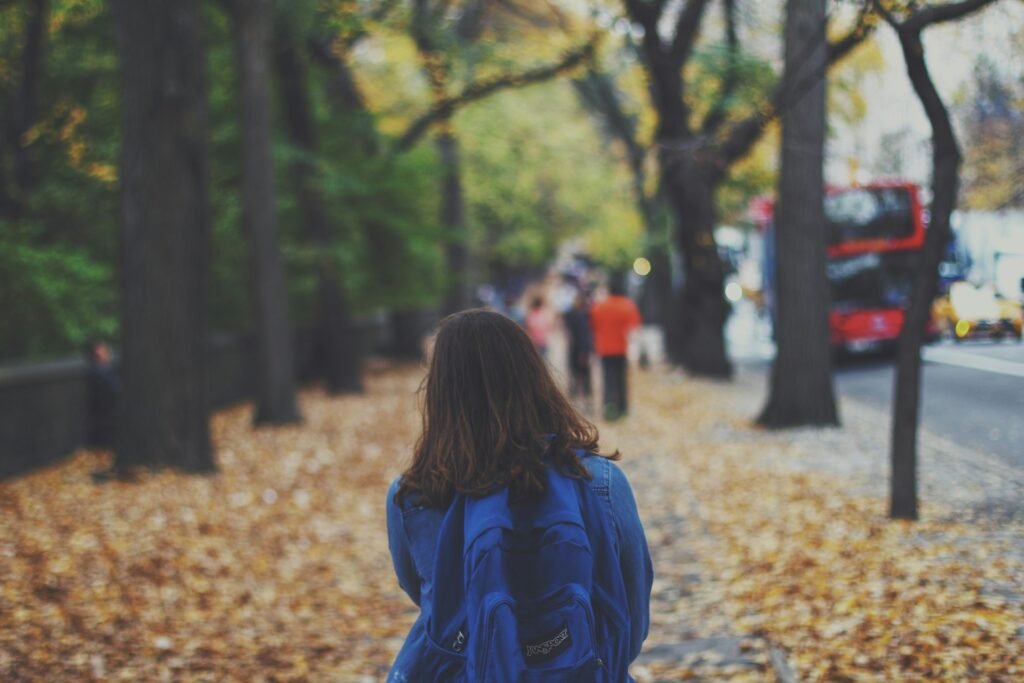 confident woman with blue backpack on street full of fallen leaves